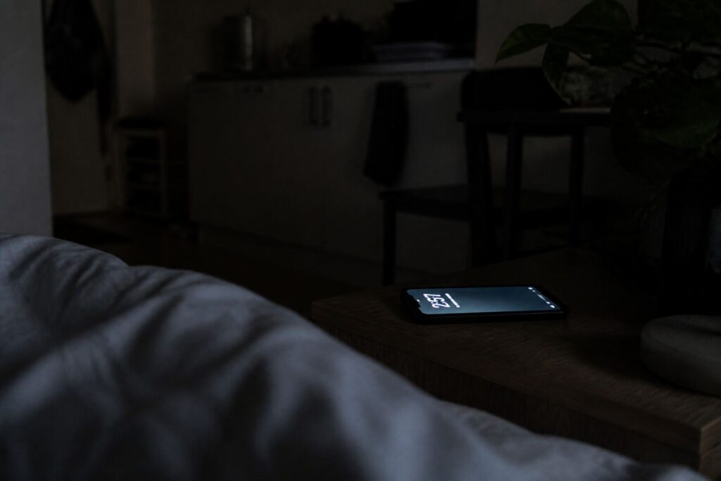 夜のワンルームでベッド脇に置かれたスマートフォンの明かり
